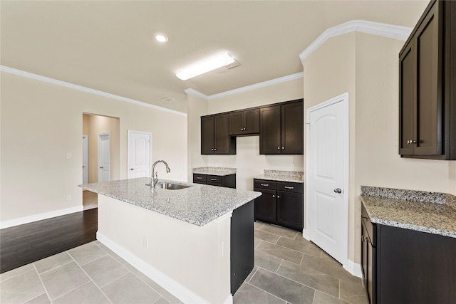 kitchen with sink, light stone counters, light hardwood / wood-style flooring, a kitchen island with sink, and ornamental molding