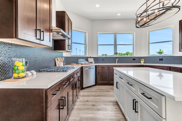 kitchen with appliances with stainless steel finishes, backsplash, ventilation hood, pendant lighting, and white cabinetry