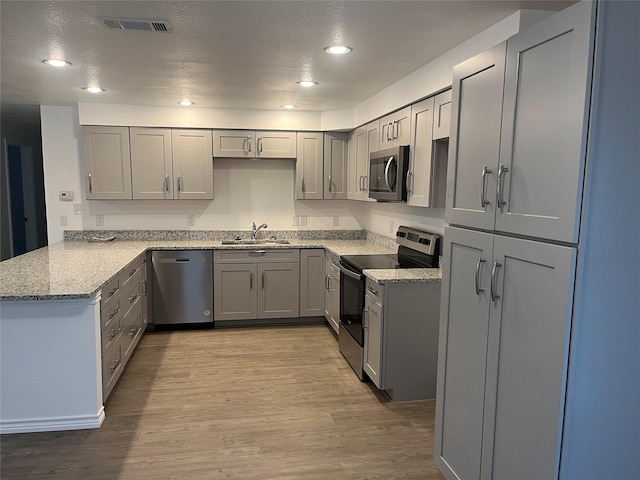 kitchen with appliances with stainless steel finishes, sink, gray cabinetry, kitchen peninsula, and light wood-type flooring