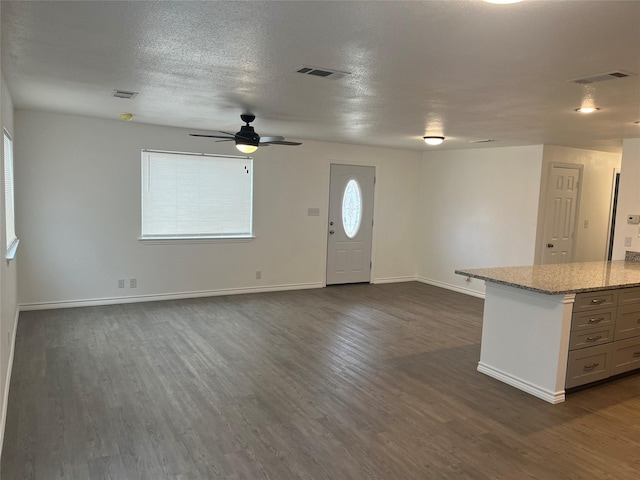 unfurnished living room featuring ceiling fan, a healthy amount of sunlight, dark hardwood / wood-style floors, and a textured ceiling