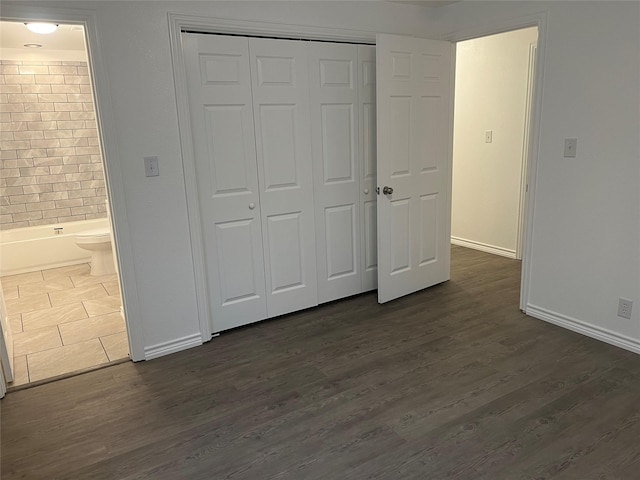 unfurnished bedroom featuring ensuite bathroom, dark hardwood / wood-style flooring, and a closet