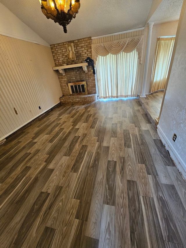 spare room featuring brick wall, lofted ceiling, a textured ceiling, dark wood-type flooring, and a fireplace