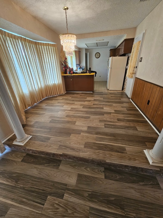 unfurnished dining area with plenty of natural light, a textured ceiling, a notable chandelier, and hardwood / wood-style floors