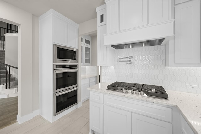 kitchen with white cabinets, tasteful backsplash, light hardwood / wood-style floors, and appliances with stainless steel finishes