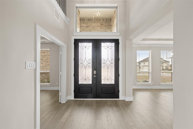 entryway featuring french doors, hardwood / wood-style floors, an inviting chandelier, and a towering ceiling