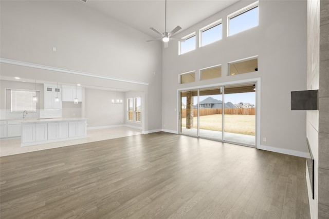 unfurnished living room featuring a towering ceiling, light hardwood / wood-style flooring, ceiling fan with notable chandelier, and a healthy amount of sunlight