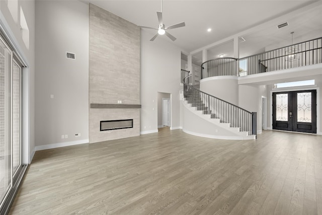 unfurnished living room with light hardwood / wood-style floors, a fireplace, ceiling fan, a high ceiling, and french doors