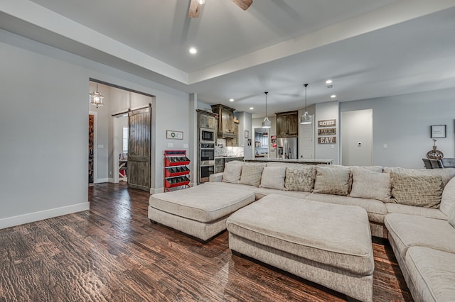 living room featuring ceiling fan, a barn door, and dark wood-type flooring