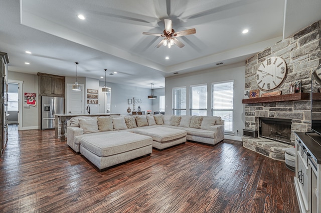 living room featuring a fireplace, ceiling fan, dark wood-type flooring, and a raised ceiling