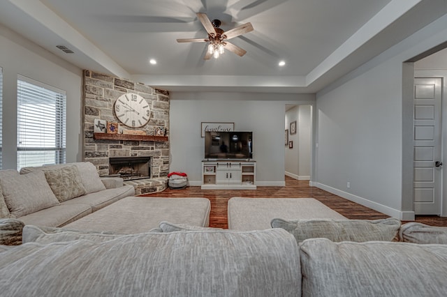 living room featuring hardwood / wood-style flooring, ceiling fan, and a stone fireplace