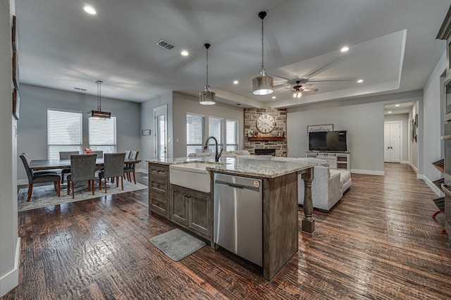 kitchen with a center island with sink, decorative light fixtures, a stone fireplace, sink, and dishwasher