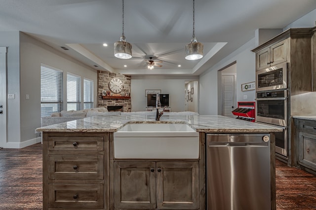 kitchen featuring a fireplace, sink, a tray ceiling, light stone counters, and appliances with stainless steel finishes