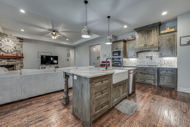 kitchen with a center island with sink, stainless steel appliances, a stone fireplace, sink, and a breakfast bar area