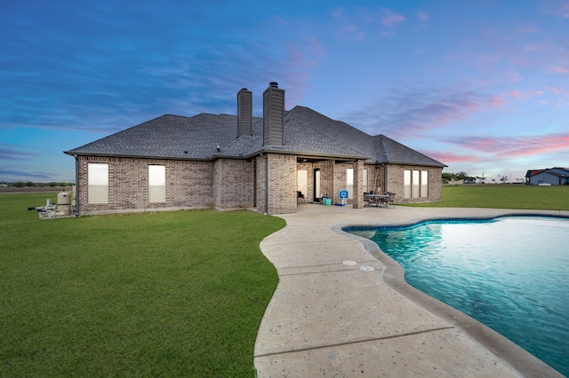 pool at dusk with a patio and a lawn