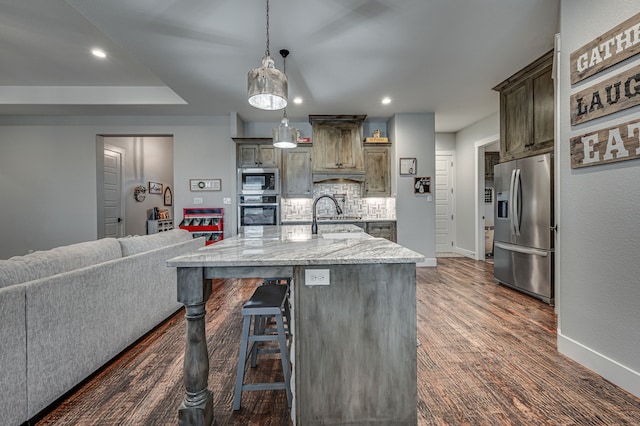 kitchen featuring a kitchen island with sink, hanging light fixtures, light stone countertops, backsplash, and appliances with stainless steel finishes