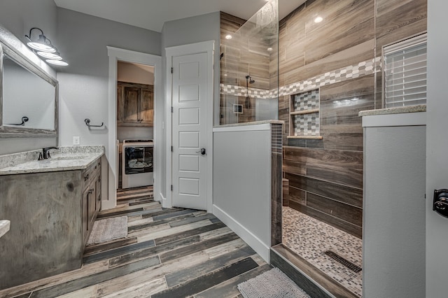 bathroom with hardwood / wood-style flooring, vanity, a tile shower, and washer / dryer