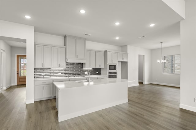 kitchen featuring dark hardwood / wood-style flooring, built in microwave, a kitchen island with sink, sink, and a notable chandelier