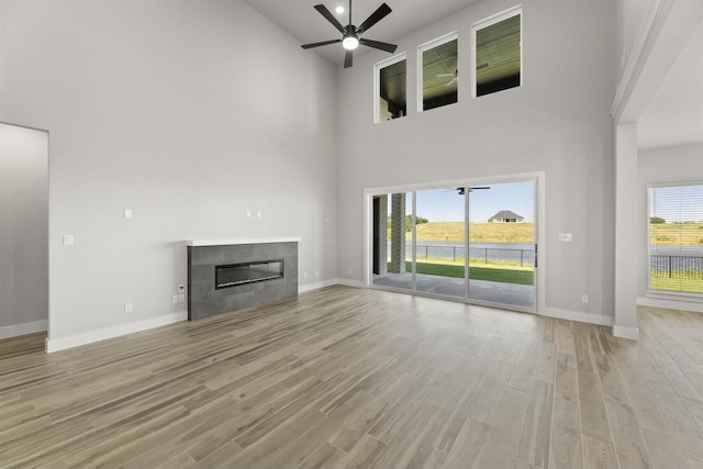 unfurnished living room with a tiled fireplace, a high ceiling, ceiling fan, and light hardwood / wood-style flooring