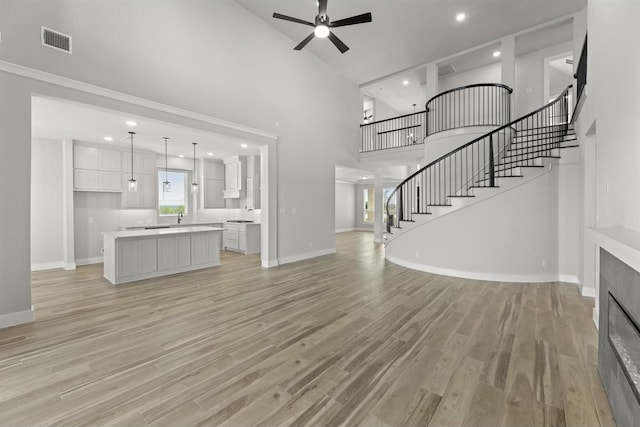 unfurnished living room with a high ceiling, ceiling fan, sink, and light hardwood / wood-style floors