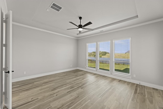 empty room featuring a raised ceiling, ornamental molding, and light wood-type flooring