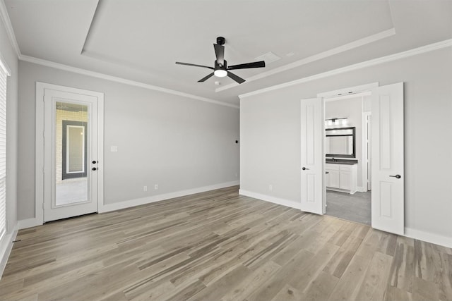 interior space with ceiling fan, connected bathroom, a tray ceiling, ornamental molding, and light wood-type flooring