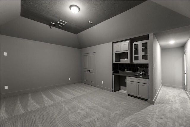 interior space featuring light carpet, sink, lofted ceiling, and a textured ceiling