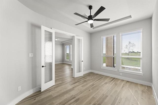 empty room with french doors, ceiling fan, a raised ceiling, and light wood-type flooring