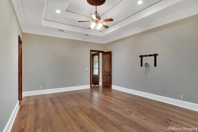 empty room featuring ceiling fan, dark wood-type flooring, ornamental molding, and a tray ceiling