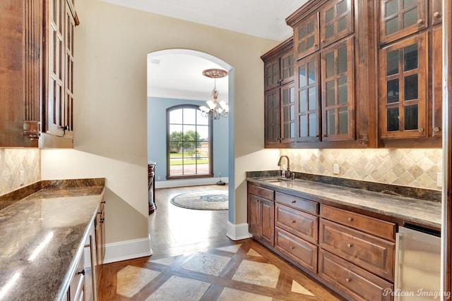 kitchen with hanging light fixtures, backsplash, sink, a chandelier, and ornamental molding