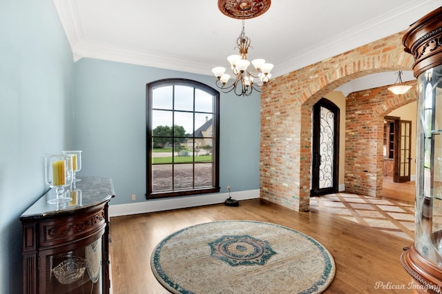 foyer with brick wall, crown molding, a chandelier, and light hardwood / wood-style flooring