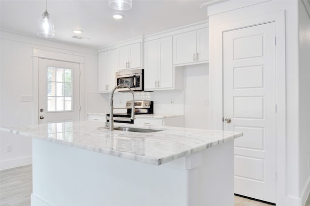 kitchen featuring appliances with stainless steel finishes, light wood-type flooring, decorative light fixtures, white cabinetry, and a kitchen island with sink