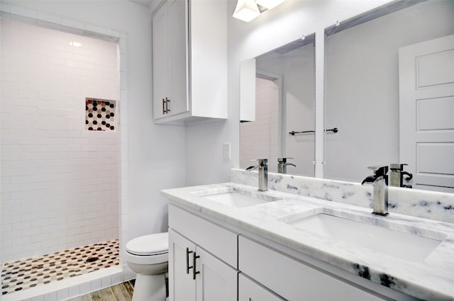 bathroom featuring dual sinks, vanity with extensive cabinet space, toilet, a tile shower, and wood-type flooring