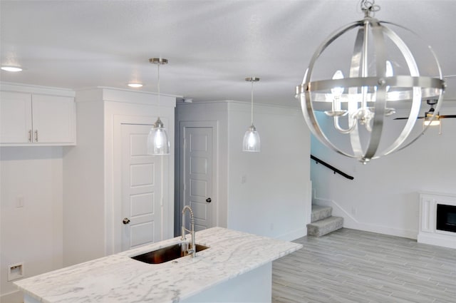 kitchen with pendant lighting, sink, white cabinets, light hardwood / wood-style floors, and light stone countertops