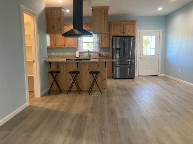 kitchen featuring light hardwood / wood-style flooring, stainless steel fridge, wall chimney range hood, a kitchen bar, and stone countertops