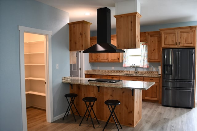 kitchen with a kitchen breakfast bar, light hardwood / wood-style flooring, black fridge, wall chimney exhaust hood, and sink