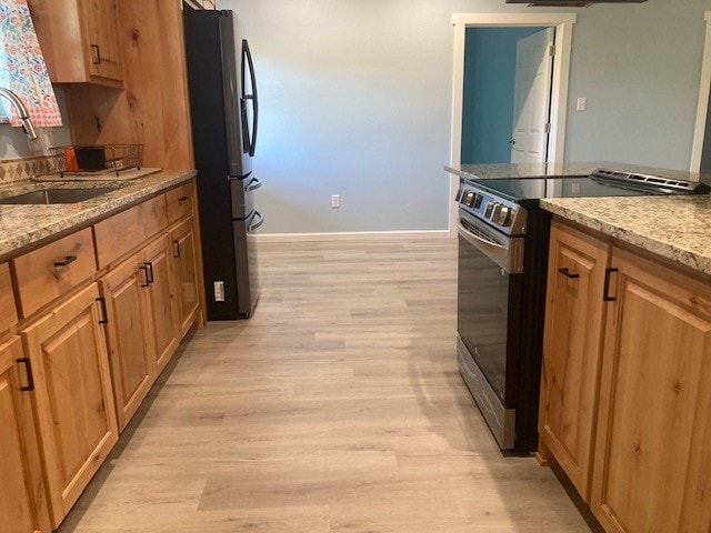 kitchen with black fridge, light stone countertops, light wood-type flooring, electric range, and sink