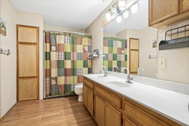 bathroom with dual vanity, toilet, hardwood / wood-style floors, and a textured ceiling