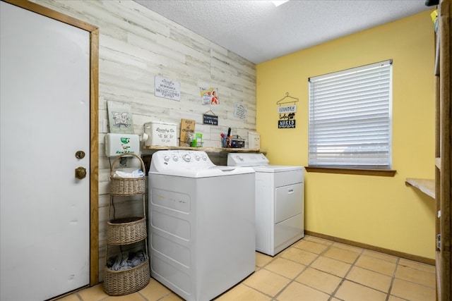 washroom with wooden walls, a textured ceiling, washer and dryer, and light tile flooring