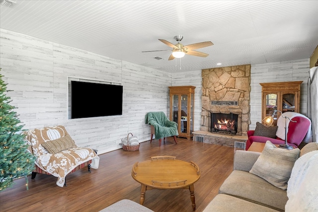 living room featuring wooden walls, a stone fireplace, wood-type flooring, and ceiling fan