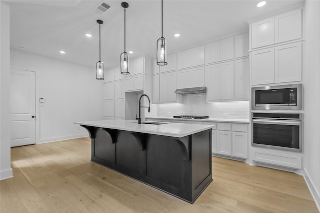 kitchen featuring an island with sink, appliances with stainless steel finishes, pendant lighting, light wood-type flooring, and white cabinetry