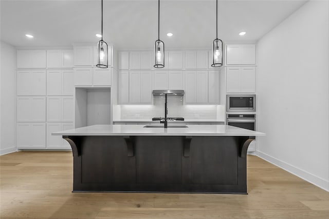 kitchen featuring stainless steel appliances, light wood-type flooring, a center island with sink, and hanging light fixtures