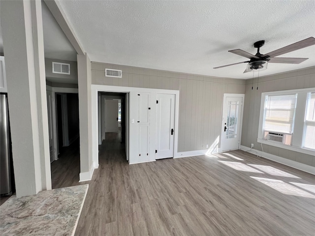 unfurnished room with ceiling fan, cooling unit, a textured ceiling, and light hardwood / wood-style floors