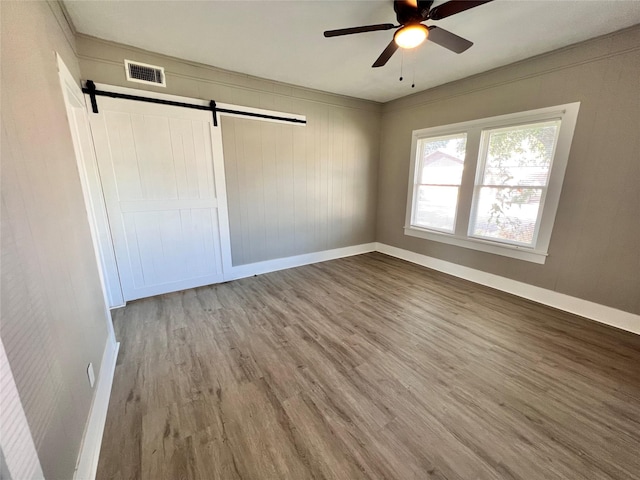 unfurnished bedroom with a closet, hardwood / wood-style flooring, a barn door, and ceiling fan