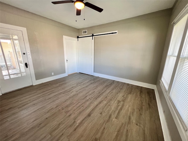 unfurnished bedroom featuring crown molding, a barn door, hardwood / wood-style floors, and ceiling fan