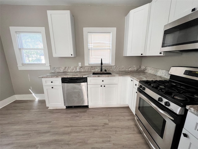 kitchen featuring sink, white cabinetry, light stone counters, stainless steel appliances, and light hardwood / wood-style floors