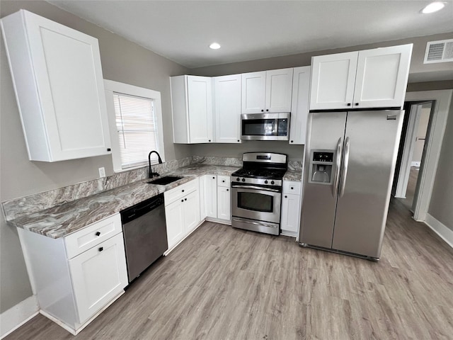 kitchen with white cabinetry, appliances with stainless steel finishes, sink, and dark stone counters