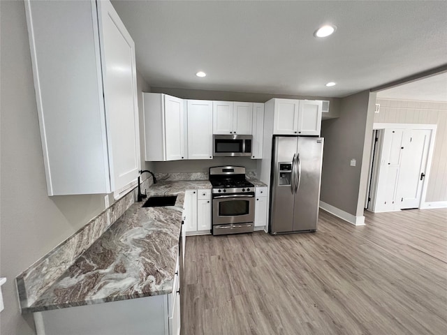 kitchen with sink, light hardwood / wood-style flooring, appliances with stainless steel finishes, light stone counters, and white cabinets