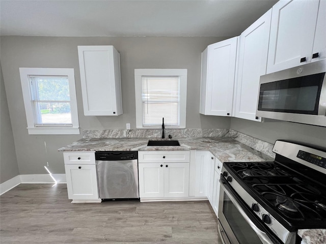 kitchen featuring appliances with stainless steel finishes, a wealth of natural light, sink, white cabinets, and light stone countertops