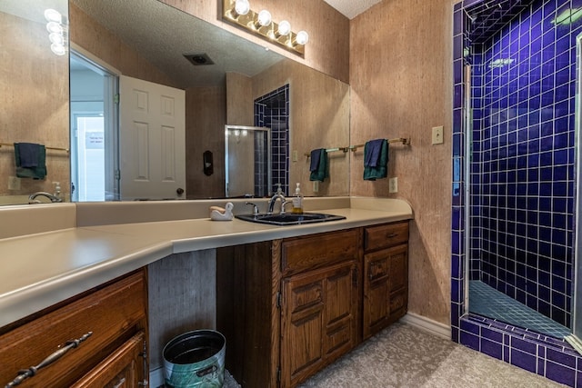 bathroom with a shower with shower door, vanity, and a textured ceiling