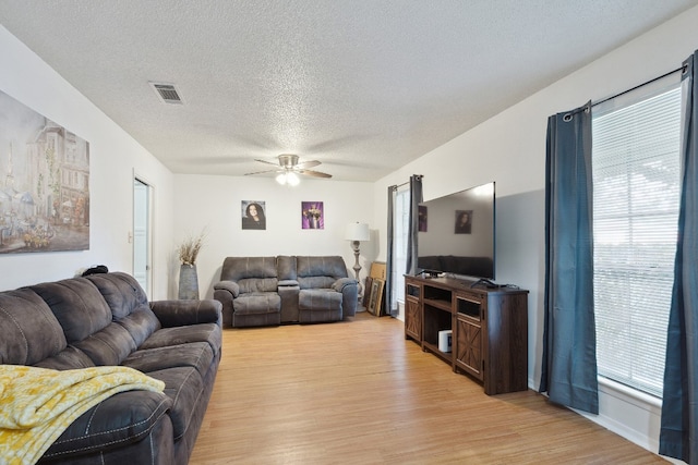 living room featuring ceiling fan, light wood-type flooring, and a textured ceiling